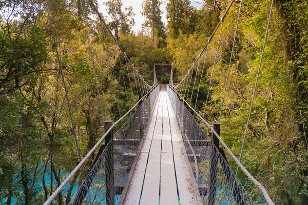 Hanging walk suspension bridge with wooden path leading to tropical forest