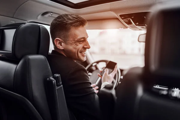 Un jeune homme souriant tenant un téléphone portable dans une voiture — Photo