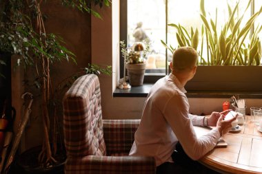 Kafede akıllı telefonlu bir adam masada oturuyor.