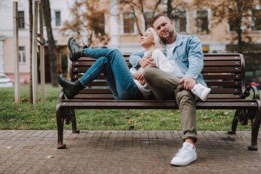 Gülümseyen mutlu kadın ve erkek günlük giysiler içinde sokak bankında otururken kucaklaşıyorlar.