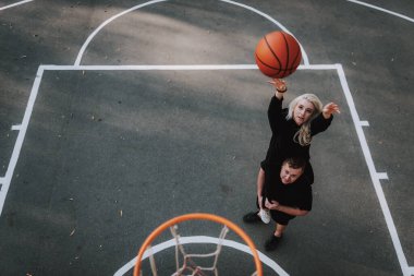 Dışarıda basketbol oynarken erkek arkadaşının omuzlarında oturan çekici bir kadın manzarası.
