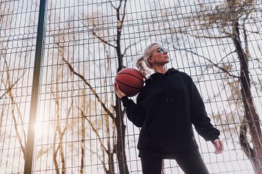 Güneşli bir günde dışarıda basketbol topuyla spor giyim sektöründe güzel bir bayan.
