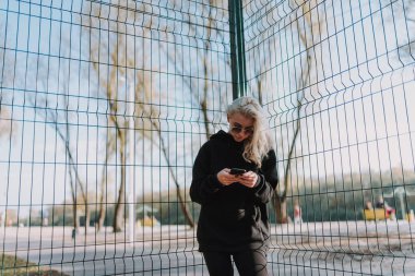 Basketbol sahasının yanında duran ve telefon kullanırken şık kıyafetler giyen güzel bayanın belini kaldırın.