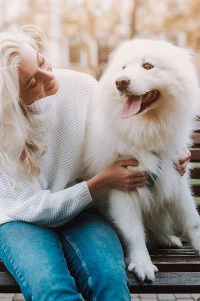 Joven Hembra Sonriente Abrazando Perro Blanco Esponjoso Mientras Está Sentada — Foto de Stock