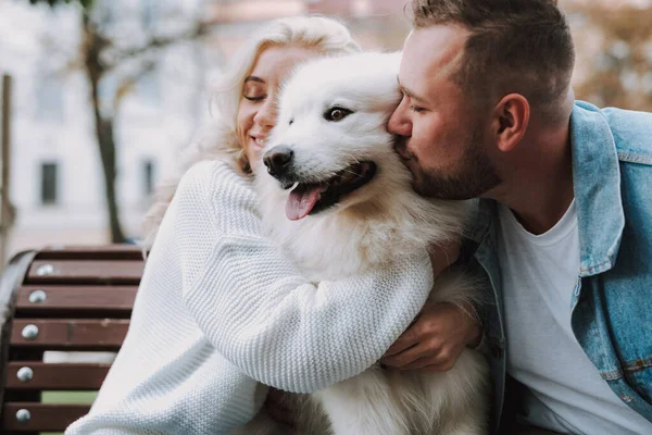 Genç bayan ve adam bir sokak bankında dinleniyor. Beyaz tüylü köpeğe sarılıp öpüşüyorlar.