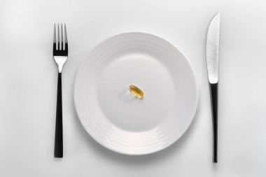 Beyaz arka planda kesicilerin yanında sarı kapsül omega 3 ile dolu beyaz kapsüllü masa ayarı. İlaç bağımlılığı ve sağlıklı beslenme kavramını temsil etmek için, ilaç endüstrisi veya ürününüz için bir illüstrasyon.