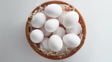 Saman dolu, içi taze ve seçilmiş beyaz tavuk yumurtalarıyla dolu bir hasır sepetin yakın çekimi. Çember dönüşü. Üst görünüm.
