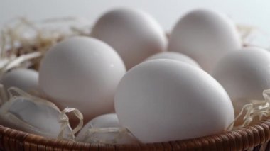 Saman dolu, içi taze ve seçilmiş beyaz tavuk yumurtalarıyla dolu bir hasır sepetin yakın çekimi. Çember dönüşü. Yan görüş. Portre oryantasyonu. Ürününüz için sağlıklı beslenme veya illüstrasyon kavramını temsil edin 