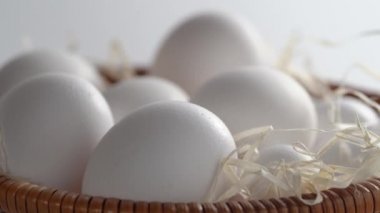 Saman dolu, içi taze ve seçilmiş beyaz tavuk yumurtalarıyla dolu bir hasır sepetin yakın çekimi. Çember dönüşü. Yan görüş. Portre oryantasyonu. Ürününüz için sağlıklı beslenme veya illüstrasyon kavramını temsil edin 