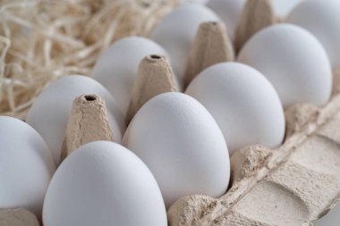 Saman ve taze ve seçilmiş beyaz tavuk yumurtalarıyla dolu bir yumurta tepsisinin yakın çekimi. Yan görüş. Portre oryantasyonu. Ürününüz için sağlıklı beslenme veya illüstrasyon kavramını temsil edin