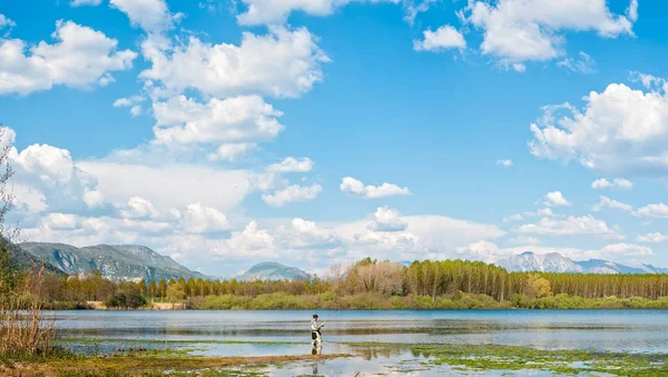 Paisaje con el hombre pescando desde la orilla del lago  . — Foto de Stock