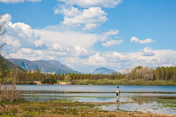 Paisaje con el hombre pescando desde la orilla del lago  . — Foto de Stock
