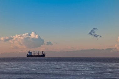 Bulutlu gün batımında gemiyle deniz manzarası.