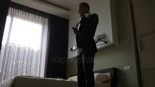 Il giovanotto si mette la giacca nella stanza della luce. Uomo elegante in costume da abito di moda che si prepara ad uscire a un ricevimento o un matrimonio . — Video Stock