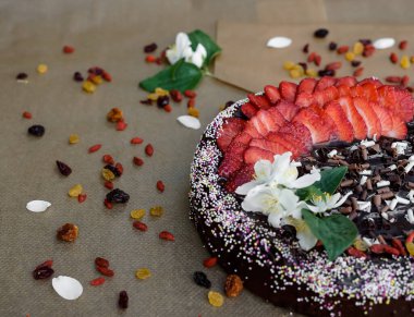 Kuru üzümlü ve kuru meyveli ev yapımı çilekli kek, üç kat bukleli çikolata, kahverengi kabartma kağıdına çikolata soslu çok renkli şeker, kuru meyve ve yasemin çiçeği. Seçici odak.