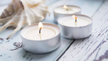 Mavi ahşap arka planda üç küçük mum ve midye kabuğu. Mumların yanındaki fetil 'e odaklan..