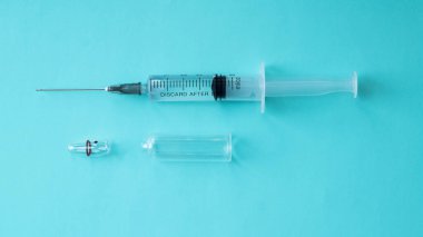 Mavi arka planda açık ampullü ilaç dolu bir şırınga. Sağlık ve tıp konsepti. Kas içi enjeksiyon. Aşı ampulde.