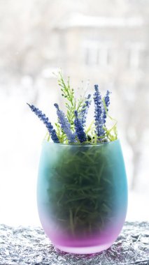 İçinde lavanta dalları ve bir kış penceresinin arka planında çimen bulunan yeşil-pembe desenli bir cam. Yapay çiçekler. Dekor konusu. İç konsept.