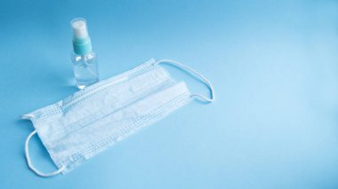 Mavi arka planda tıbbi maskesi olan şeffaf bir şişede antiseptik. Virüslere karşı önlem ve koruma. Sağlık ve ilaç servisi. Coronavirus. Covid - 19.