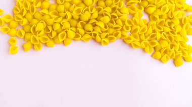 Kabuk şeklinde serpiştirilmiş makarna ve pembe arka planda katkı maddeleri..