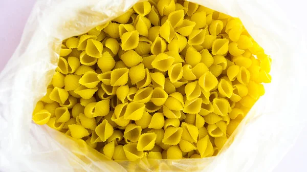 Maccheroni in una borsa sotto forma di conchiglie con additivi primo piano su fondo rosa . — Foto Stock