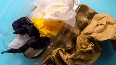 Plastik, kağıt, karton, selofan ve demirden yapılmış çöpler mavi arka planda. 