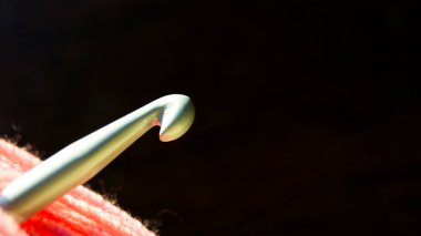 Örgü, hobi, dikiş. Yakın plan örgü kancası pembe ipliğin içinde koyu bir arka planda duruyor. Mesaj için yer. Boşluğu kopyala.