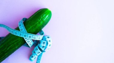 Diyet, sağlıklı beslenme, yiyecek ve kilo verme konsepti. Sebze besin. Sağlığınıza. Pembe arka planda mezurayla sarılı yeşil salatalık. Mesaj için yer. Uzayı kopyala Seçici odak.