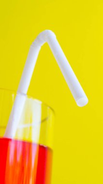 Beyaz plastik tek kullanımlık pipet ve sarı arka planda kırmızı yaz kokteyli. Tazeleyici içecek. Sıcak mevsim. Alkolsüz içecek. Düzgün beslenme. Seçici odak.