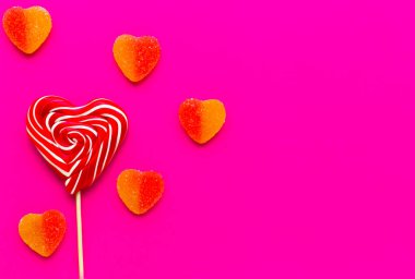 Çizgili vida kırmızı ve beyaz kalp şeklinde şeker ve pembe arka planda şekerli marmelat. Tatlı ikram. Lezzetli bir hediye. Kartpostal için kullan. Aşk konsepti. Sevgililer Günü.