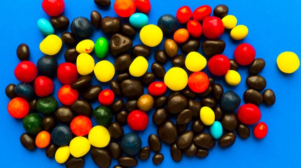 Verspreid helder multi-gekleurde snoepjes in de vorm van jelly beans op een blauwe achtergrond. Rozijnen in chocolade, pinda 's in chocolade. Kinderfeestdagen. Mooie traktatie. Cadeau en promotie. Selectieve focus. — Stockfoto