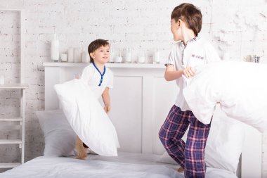 İki erkek kardeş, pijamalı kardeşler yatakta yastık savaşı yapıyorlar.