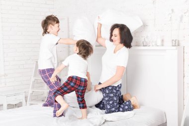 Anne ve iki oğul evde yastık kavgası yapıyor, kardeşler çocuklar yastık kavgası yapıyor anneleriyle gülüyorlar.