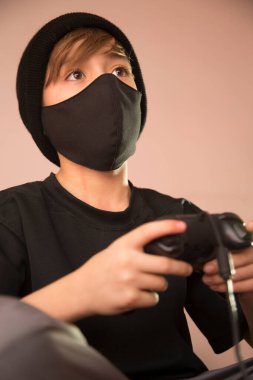 Maskeli bir çocuğun portresi, ağzı kapalı bir çocuk, önleme maskesi, kovid 19 hastalıklarından kaçınmak için. video oyunları oynanıyor