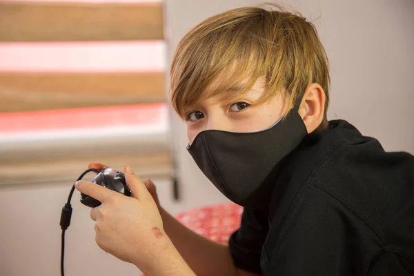 Maskeli bir çocuğun portresi, ağzı kapalı bir çocuk, önleme maskesi, kovid 19 hastalıklarından kaçınmak için. video oyunları oynanıyor