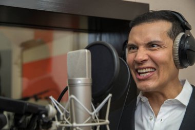 Aktör ve radyo spikeri kulaklıkları ve mikrofonuyla film kaydediyor, radyo sahnesi çekiyor ve şarkı söylüyor.