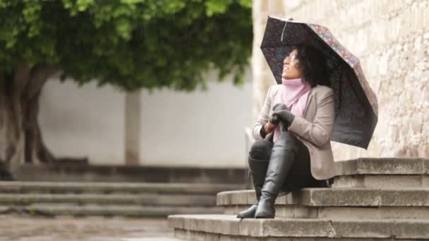 ラテン語の女の子とブルネットの肌と巻き毛 雨の中で 瞬間を楽しんで 電話に答え 人生で笑顔 — ストック動画