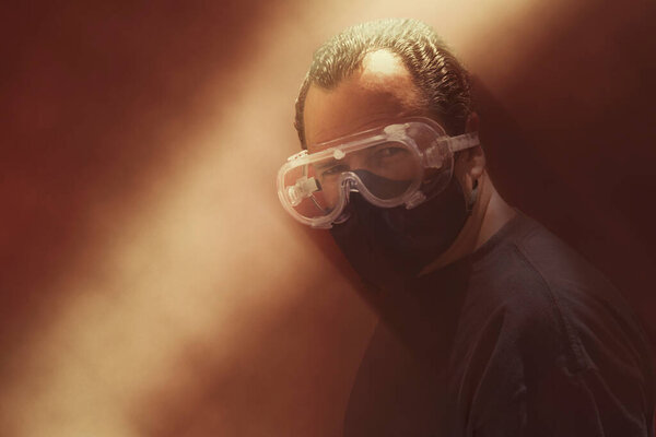 Белый человек в красном фоне, в очках и защитной маске, в серьезном настроении, злой, вдумчивый, собирается напасть, наблюдая за своей жертвой, чтобы выследить ее
