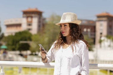 Teknoloji kullanan güzel bir kız. Şapkalı ve gözlüklü Latin bir kız. Cep telefonuna danışıyor.