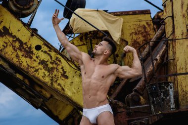 Beyaz şortlu seksi adam çıplak gövdeli atletik vücut geliştirme figürünü sarı kazıcı arka planına karşı gösteriyor.