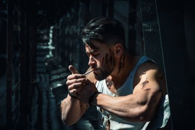 Moladaki adam sigara içiyor, sakallı ve spor figürlü.