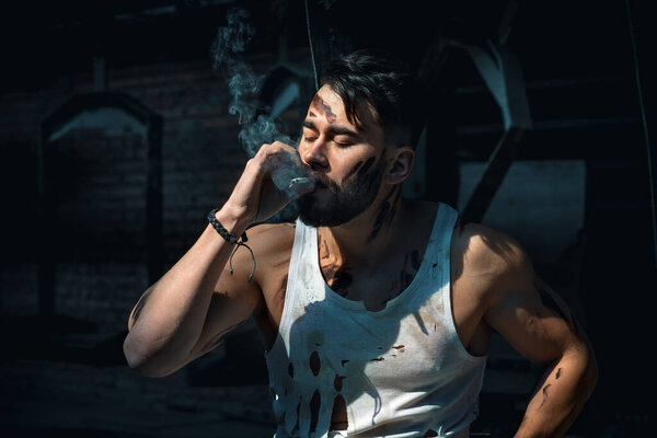 Парень на перерыве курит сигарету, бородатый мужчина со спортивной фигурой
