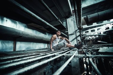 Adam endüstriyel tesislerin borularında oturuyor, gaz boruları, insanların çalıştığı üretim fabrikası, sporcu adam.