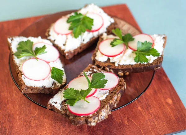 rectangular sandwiches with butter, cheese and radish on a black plate. side view