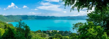 Panoramic view of the beautiful lake of Coatepeque in El Salvador, with a blue sky, in the season where its waters are turquoise and most of its mountains and vegetation are green. clipart