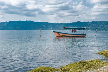 İlopango gölünün kıyısından gölün berrak sularında ve güzel yeşil dağların arkasında bir tekne görünüyor. El Salvador