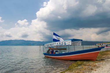 İlopango gölünün kıyısından gölün berrak sularında ve güzel yeşil dağların arkasında bir tekne görünüyor. El Salvador