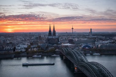 Günbatımında Köln ufuk çizgisi, Köln Şeytan Üçgeni manzarası. Gotik Katedral Dom, Hohenzollern Köprüsü ve Ren Nehri 'nden geçen büyük bir tekne.