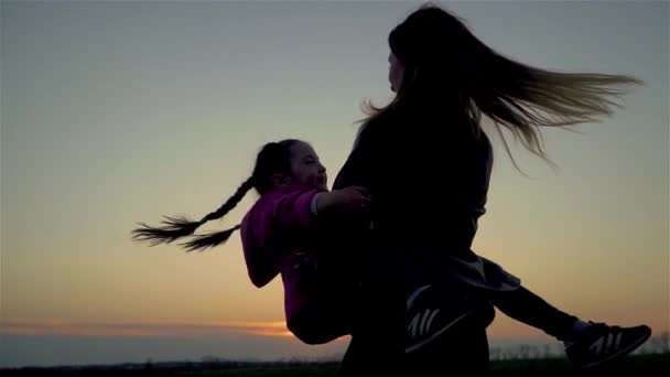 Mother holds her daughter in arms and they are spinning and hair is flying on wind at sunset in slow motion — Stock Video