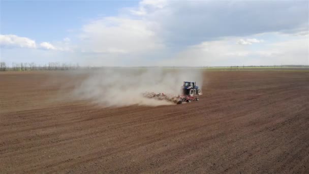 Filmato aereo del moderno trattore blu con aratro rosso arare o coltivare grande campo sotto cielo nuvoloso piovoso — Video Stock